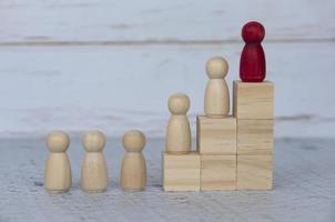 Wooden people figures on top of wooden blocks with red figure leading the rest. Business concept photo