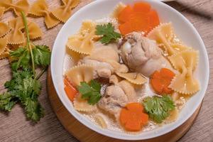 Macaroni soup with chicken thighs in clear broth with carrots.on an rustic old wood background. photo