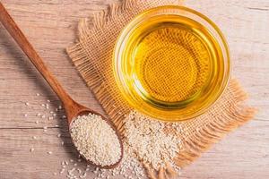 aceite de sésamo en un bol y semillas de sésamo blanco sobre fondo de madera foto