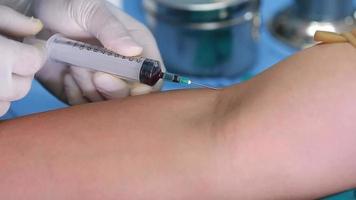 technicien de laboratoire tenant un échantillon de tube de sang pour étude, piquant une seringue à aiguille dans le bras du patient prélevant un échantillon de sang pour un test sanguin. video