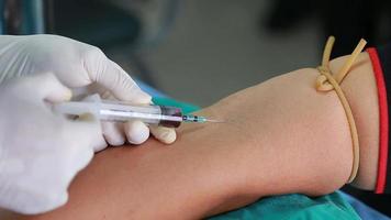 technicien de laboratoire tenant un échantillon de tube de sang pour étude, piquant une seringue à aiguille dans le bras du patient prélevant un échantillon de sang pour un test sanguin. video