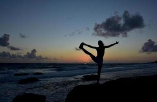 postura de equilibrio de la silueta del amanecer a lo largo de la costa foto