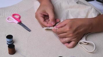 main d'une couturière au travail avec du tissu en tissu. mère coud une belle robe pour sa petite fille à la main, gros plan. la main de femme coud des coutures avec des fils bleus. video