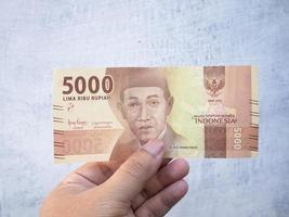a man holding a 5000 rupiah banknote in his hand photo
