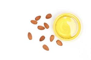 Clear yellow almond oil in a clear bowl and several almonds on a white background.top view, flat lay, top-down. photo
