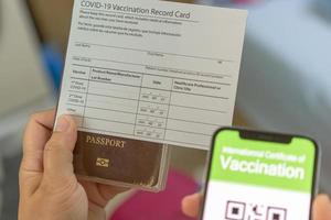 Woman in travel clothes wearing a medical mask showing covid-19 vaccination record card and passport and pink suitcase. Travel concept with vaccination. photo