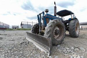 tractor azul estacionado en un claro en preparación para la capa superior del suelo y un hermoso cielo azul en el fondo. el concepto de una excavadora prepara la capa superior del suelo para la construcción. foto