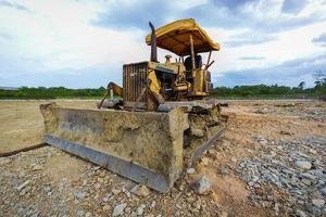 Bulldozer sobre orugas amarillo estacionado en un claro en preparación para la capa superior del suelo y un hermoso cielo azul en el fondo. el concepto de una excavadora prepara la capa superior del suelo para la construcción. foto