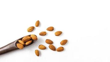 The almonds are in a brown wooden spoon and several seeds around which are on isolate a white background. photo