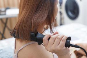 Behind the scenes of a reddish-haired woman straightening her hair with a straightener on her bed in the house. photo