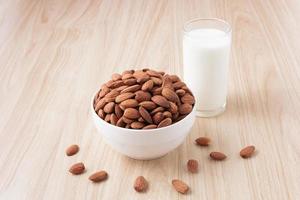 Almond nuts in a white bowl and milk in glass on wood background with nuts around the bowl.selective focus.front view. photo