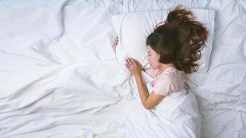 mujer joven durmiendo bien en la cama abrazando una suave almohada blanca. adolescente descansando. concepto de buenas noches de sueño. chica en pijama duerme en una cama en una habitación blanca por la mañana. tono cálido. foto