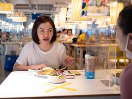 Asian woman sitting separated in restaurant eating food with table shield plastic partition to protect infection from coronavirus covid-19 photo