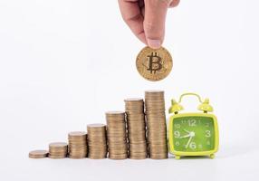 mano sosteniendo bitcoin y muchas monedas y reloj para ahorrar dinero concepto sobre fondo blanco foto
