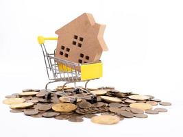 House model in mini shopping cart with stack of coins money on wooden table for residential investment