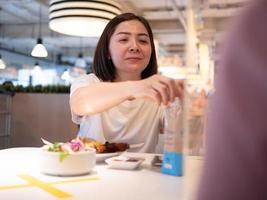 Asian woman sitting separated in restaurant eating food with table shield plastic partition to protect infection from coronavirus covid-19 photo