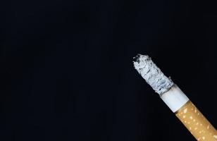 Cigarrillo encendido con humo sobre fondo negro foto