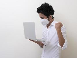 Business man in medical face mask works on laptop at home photo