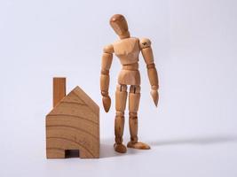 hombre se inclinó contra el modelo de una casa aislada sobre fondo blanco. concepto con una marioneta de madera foto