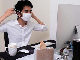 Young Asian boy wearing face mask working on laptop computer during coronavirus pandemic photo