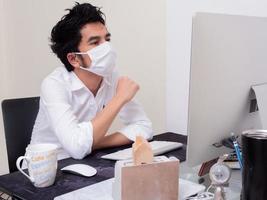 joven asiático con mascarilla trabajando en una computadora portátil durante la pandemia del coronavirus foto