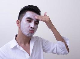 Asian handsome young man applying cream at his face with smiley face, Skin care concept photo