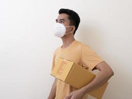 Happy delivery service employee in medical face mask carry cardboard box in hand photo