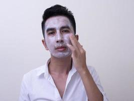 Asian handsome young man applying cream at his face with smiley face, Skin care concept photo