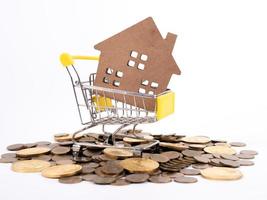 House model in mini shopping cart with stack of coins money on wooden table for residential investment photo