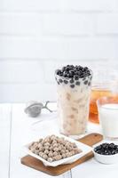 Bubble milk tea with tapioca pearl topping ingredient, famous Taiwanese drink on white wooden table background in drinking glass, close up, copy space photo