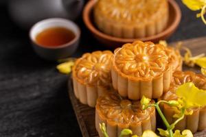 Mooncake, Moon cake for Mid-Autumn Festival, concept of traditional festive food on black slate table with tea and yellow flower, close up, copy space. photo