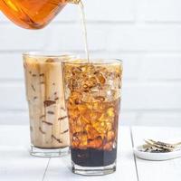 Making bubble tea, pouring blend milk tea into brown sugar pattern drinking glass cup on white wooden table background, close up, copy space photo