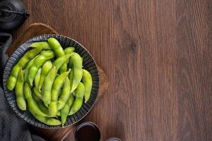 Fresh cooked boiled edamame in a plate on wooden tray and table background, healthy protein food concept. photo