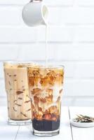 Making bubble tea, pouring blend milk tea into brown sugar pattern drinking glass cup on white wooden table background, close up, copy space photo