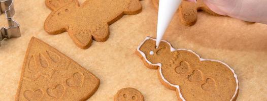 mujer joven está decorando galletas de casa de pan de jengibre de navidad en casa con cobertura de glaseado en bolsa de hielo, primer plano, estilo de vida. foto