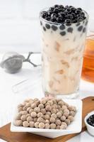 Bubble milk tea with tapioca pearl topping ingredient, famous Taiwanese drink on white wooden table background in drinking glass, close up, copy space photo