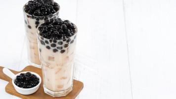 Bubble milk tea with tapioca pearl topping, famous Taiwanese drink on white wooden table background in drinking glass, close up, copy space photo
