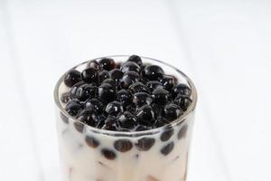 Making bubble tea, pouring blend milk tea into brown sugar pattern drinking glass cup on white wooden table background, close up, copy space photo