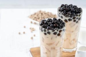 Bubble milk tea with tapioca pearl topping ingredient, famous Taiwanese drink on white wooden table background in drinking glass, close up, copy space photo