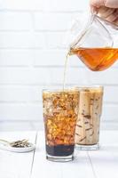 Making bubble tea, pouring blend milk tea into brown sugar pattern drinking glass cup on white wooden table background, close up, copy space photo