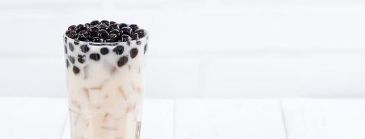 Bubble milk tea with tapioca pearl topping, famous Taiwanese drink on white wooden table background in drinking glass, close up, copy space photo