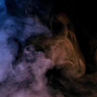 Conceptual image of multi-colored smoke isolated on dark black background and wooden table. photo