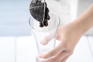 hacer té de burbujas, sacar y verter bolas de burbujas de perlas de tapioca con sabor a azúcar moreno cocido en una taza sobre fondo de mesa de madera blanca, cerrar, copiar espacio. foto