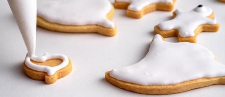 Close up of decorating cute Halloween cookies with frosting in icing bag. photo