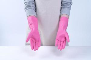 una joven ama de llaves en delantal lleva guantes rosas para limpiar la mesa, concepto de prevención de infecciones por virus, servicio de limpieza, cierre. foto