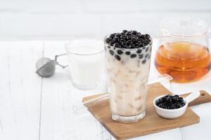 Bubble milk tea with tapioca pearl topping, famous Taiwanese drink on white wooden table background in drinking glass, close up, copy space photo