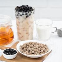 Bubble milk tea with tapioca pearl topping ingredient, famous Taiwanese drink on white wooden table background in drinking glass, close up, copy space photo