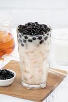 Bubble milk tea with tapioca pearl topping, famous Taiwanese drink on white wooden table background in drinking glass, close up, copy space photo