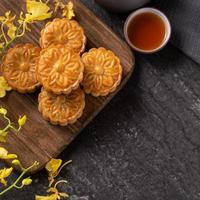 Mooncake, Moon cake for Mid-Autumn Festival, concept of traditional festive food on black slate table with tea and yellow flower, close up, copy space. photo