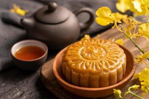 Mooncake, Moon cake for Mid-Autumn Festival, concept of traditional festive food on black slate table with tea and yellow flower, close up, copy space. photo